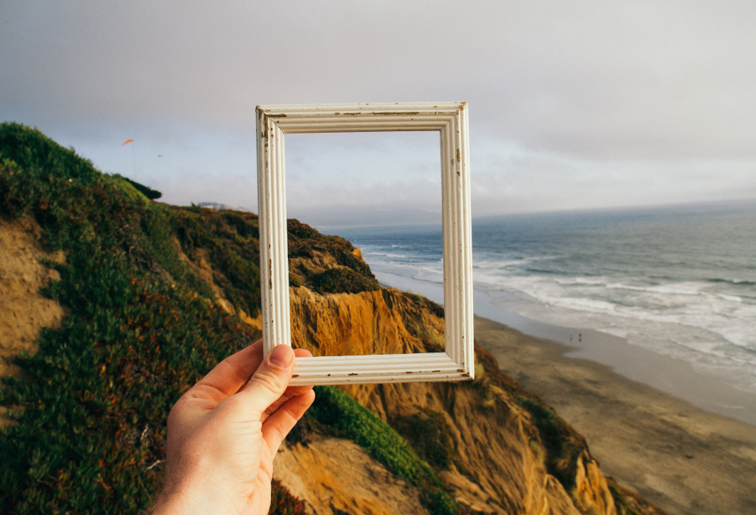 Person holding frame against cliff sea landscape